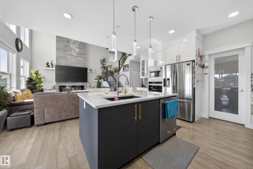 Open-concept kitchen featuring a dark blue island with gold hardware, a white countertop, and pendant lighting - 1927 18 Street, Edmonton, AB 