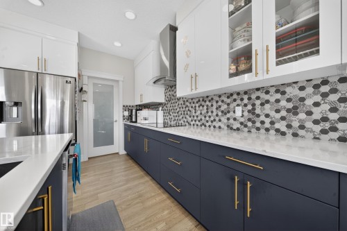 Kitchen featuring white upper cabinetry, navy blue lower cabinetry with gold-tone hardware, and light-toned wood-finish flooring - 1927 18 Street, Edmonton, AB 