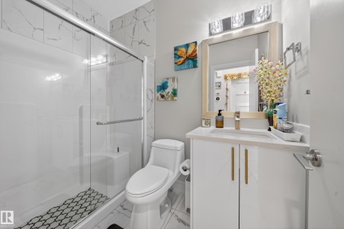 Bathroom featuring a glass-enclosed shower with subway tile surround, a white vanity with gold-tone hardware, a rectangular undermount sink, and a framed mirror - 1927 18 Street, Edmonton, AB 