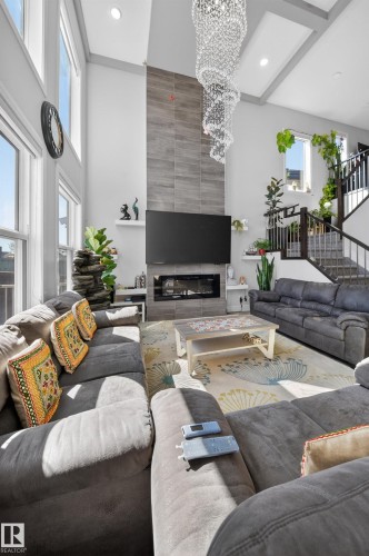 Two-story living area featuring vaulted ceilings with exposed beams, an elegant crystal chandelier, a floor-to-ceiling tile fireplace surround, and a built-in electric fireplace - 1927 18 Street, Edmonton, AB 