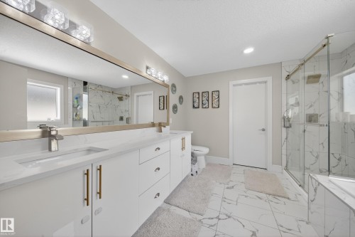 Dual vanity with integrated sinks and brushed brass hardware, complemented by an expansive mirror and overhead vanity lighting - 1927 18 Street, Edmonton, AB 