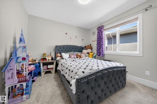 Carpeted bedroom featuring a large window with white trim, light gray walls, a built-in overhead light fixture, and white baseboards - 1927 18 Street, Edmonton, AB 