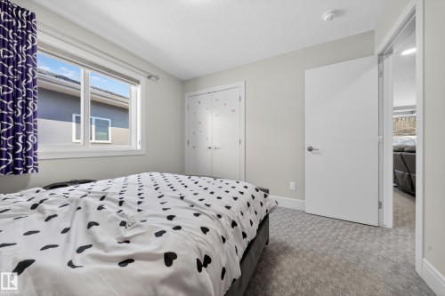 Neutral wall tones enhance this bedroom, featuring a large window with white trim, a double-door closet, and light-toned patterned carpeting - 1927 18 Street, Edmonton, AB 