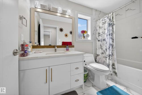 Bathroom featuring a white vanity with gold-tone hardware, a rectangular mirror, and a three-light fixture - 1927 18 Street, Edmonton, AB 