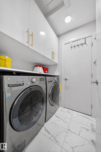 Laundry area featuring white cabinetry with gold-tone hardware, a light-colored countertop, and a patterned tile floor - 1927 18 Street, Edmonton, AB 