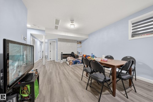 Light-toned wood-finish flooring extends throughout this expansive room, featuring a built-in recessed shelf, a window with horizontal blinds, and a patterned accent wall - 1927 18 Street, Edmonton, AB 