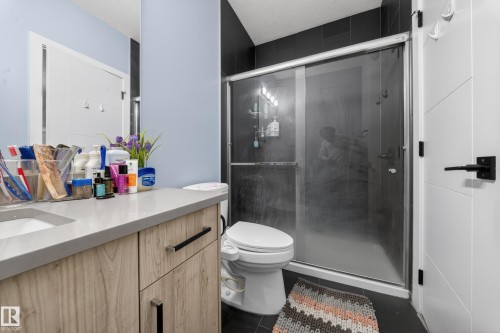 Modern bathroom featuring a wood-finish vanity with a light-toned countertop, an integrated sink, and dark hardware - 1927 18 Street, Edmonton, AB 