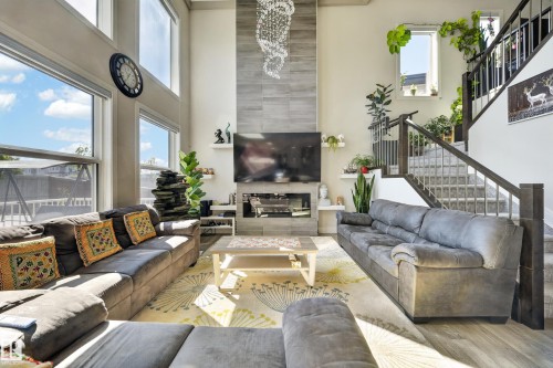 Two-story living area featuring a full-height tile fireplace surround, large windows, a contemporary chandelier, built-in shelving, and wood-finish flooring - 1927 18 Street, Edmonton, AB 