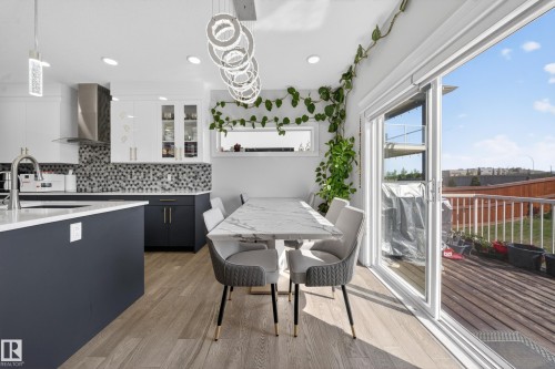 Modern kitchen featuring a mosaic tile backsplash, stainless steel range hood, white and dark-toned cabinetry, and a light wood-finish floor - 1927 18 Street, Edmonton, AB 