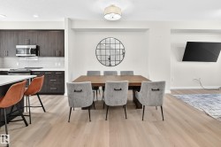 Open-concept dining area with wood-finish flooring, a contemporary ceiling fixture, a built-in wall niche, and a contrasting kitchen island with bar seating - 