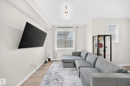 Bright living area featuring light wood-finish flooring, a contemporary ceiling light fixture, and white trim molding - 118 655 Watt Boulevard Sw, Edmonton, AB 