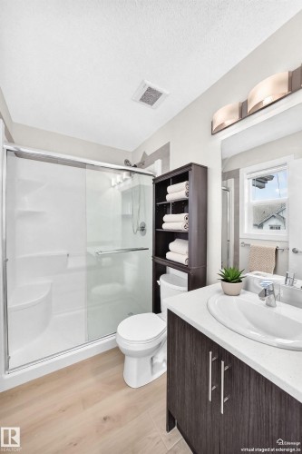 Contemporary bathroom featuring a wood-finish vanity with a white countertop and undermount sink, a shower stall with a sliding glass door, light wood-finish flooring, and a window with natural light - 118 655 Watt Boulevard Sw, Edmonton, AB 