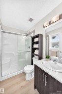 Contemporary bathroom featuring a wood-finish vanity with a white countertop and undermount sink, a shower stall with a sliding glass door, light wood-finish flooring, and a window with natural light - 