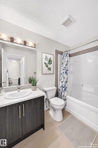 Contemporary bathroom featuring a dark wood-finish vanity with a white countertop and undermount sink, a white toilet, and a white tub with a shower - 118 655 Watt Boulevard Sw, Edmonton, AB 