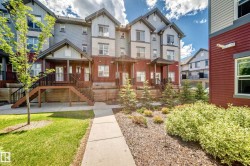 Multi-level townhome featuring a covered entrance porch, exterior stairs with dark railings, and a landscaped front yard with grass and plantings - 
