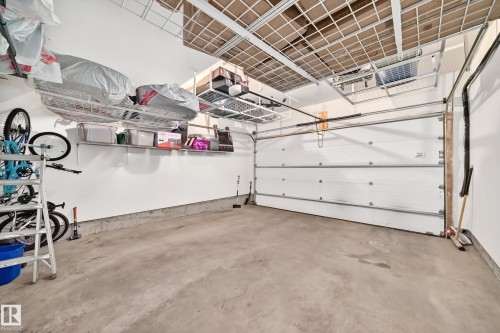 Spacious garage with concrete flooring, white walls, overhead storage racks, and wall-mounted shelving for organization - 118 655 Watt Boulevard Sw, Edmonton, AB 
