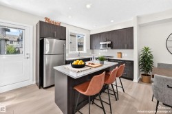 Modern kitchen featuring dark wood-finish cabinetry, stainless steel appliances, a center island with a light countertop, and light wood-finish flooring - 