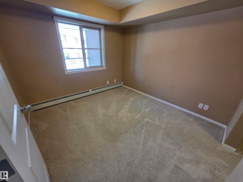 Carpeted interior space featuring a window with white trim, baseboard heating, neutral wall paint, and white baseboards - 319 5816 Mullen Place, Edmonton, AB 