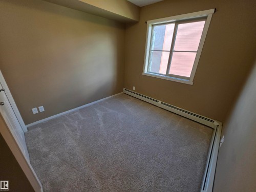 Carpeted room with a double-pane window, baseboard heating, and neutral wall tones - 319 5816 Mullen Place, Edmonton, AB 