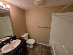 Bathroom featuring a dark vanity with an integrated sink, chrome faucet, and a large mirror with overhead vanity lighting - 