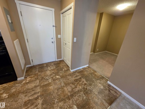 Entryway featuring wood-finish flooring, a solid white entry door with chrome hardware, and a built-in closet with bifold doors - 319 5816 Mullen Place, Edmonton, AB 