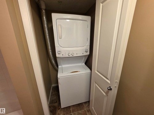 Dedicated laundry closet featuring a white stacked washer and dryer unit, flexible metal dryer vent, and durable tiled flooring - 319 5816 Mullen Place, Edmonton, AB 