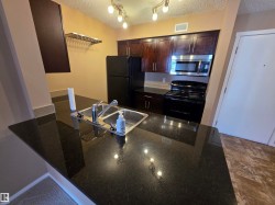 Kitchen featuring a dark granite countertop with a double-basin sink, rich wood-finish cabinetry, and black appliances including a refrigerator and range - 