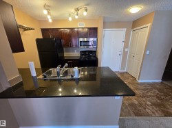 Kitchen featuring dark wood-finish cabinetry, black appliances, a double basin stainless steel sink, and a black granite-look countertop island - 