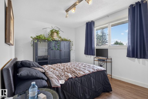 Bedroom featuring wood-finish flooring, a double window, track lighting, and a built-in dark wood wardrobe with mirrored panels - 7539 149A Avenue, Edmonton, AB 