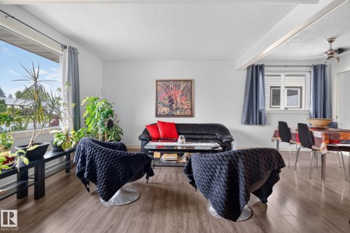 Open-concept living area with wood-finish flooring, a broad picture window, and a textured white ceiling - 7539 149A Avenue, Edmonton, AB 