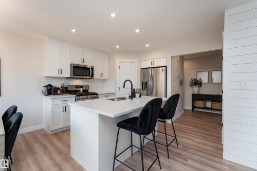 Contemporary kitchen featuring white shaker cabinetry, stainless steel appliances, a subway tile backsplash, and an island with an integrated sink and matte black faucet - 584 Meadowview Drive, Fort Saskatchewan, AB 