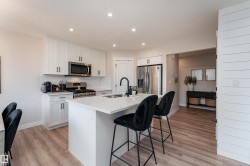 Contemporary kitchen featuring white shaker cabinetry, stainless steel appliances, a subway tile backsplash, and an island with an integrated sink and matte black faucet - 