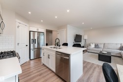 Open-concept living area featuring a kitchen island with sink, stainless steel appliances, white subway tile backsplash, recessed lighting, and wood-finish flooring - 