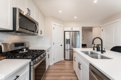 Modern kitchen featuring white cabinetry, stainless steel appliances, a subway tile backsplash, light wood-finish flooring, and recessed lighting - 