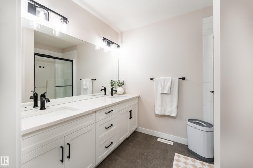 Double vanity featuring white cabinetry, integrated sinks, black hardware, and an expansive mirror - 584 Meadowview Drive, Fort Saskatchewan, AB 