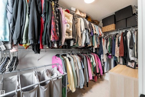 Walk-in closet featuring built-in wire shelving, multiple hanging rods, and a light wood-finish storage unit - 584 Meadowview Drive, Fort Saskatchewan, AB 