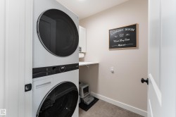 Dedicated laundry area featuring stacked front-load appliances, a white wall-mounted shelf, and a white storage cabinet with black hardware - 