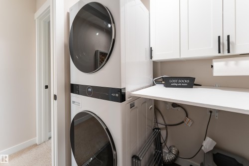 Laundry area featuring a stacked washer and dryer, white cabinetry with matte black hardware, and a white countertop - 584 Meadowview Drive, Fort Saskatchewan, AB 