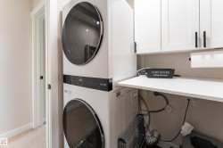 Laundry area featuring a stacked washer and dryer, white cabinetry with matte black hardware, and a white countertop - 