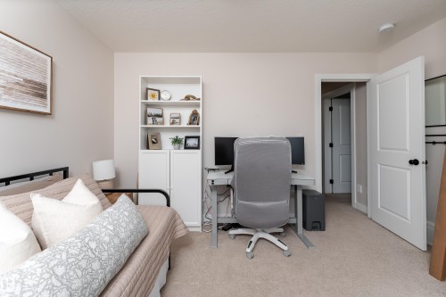 Carpeted room featuring a white built-in bookshelf with cabinet storage, a desk area, and a white panel door with black hardware - 584 Meadowview Drive, Fort Saskatchewan, AB 