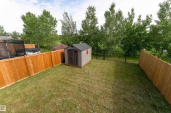 Expansive grassy backyard featuring a storage shed with double doors, wood panel fencing, and a black chain-link fence - 