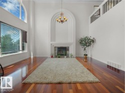 Two-story living area featuring wood-finish flooring, a prominent fireplace with an arched mantel, and a dual-level window arrangement with arched transom - 