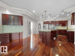 Spacious kitchen featuring rich wood-finish cabinetry, a central island with integrated seating, recessed lighting, and pendant fixtures - 