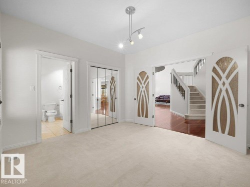 Neutral tone carpeted room with track lighting, featuring decorative paneled double doors and a mirrored closet - 2423 Tegler Green, Edmonton, AB 