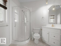 Bathroom featuring a curved glass shower enclosure, white vanity with integrated sink, arched mirror, and track lighting - 