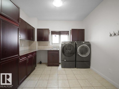 Laundry area featuring extensive dark wood cabinetry, light tile flooring, solid surface countertops, and a utility sink - 2423 Tegler Green, Edmonton, AB 