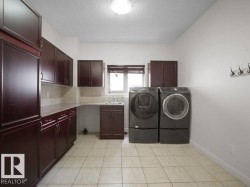 Laundry area featuring extensive dark wood cabinetry, light tile flooring, solid surface countertops, and a utility sink - 