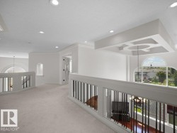 Open loft area featuring recessed lighting, a decorative ceiling fixture, arched windows, light-toned carpeting, and white balusters with dark vertical spindles - 
