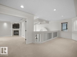 Carpeted room featuring a built-in fireplace with a tiled surround, recessed lighting, crown molding, and a partial balustrade - 