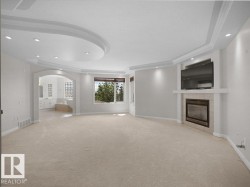 Spacious room featuring a tray ceiling with recessed lighting, a fireplace with a stone surround, and an arched doorway leading to an additional space - 